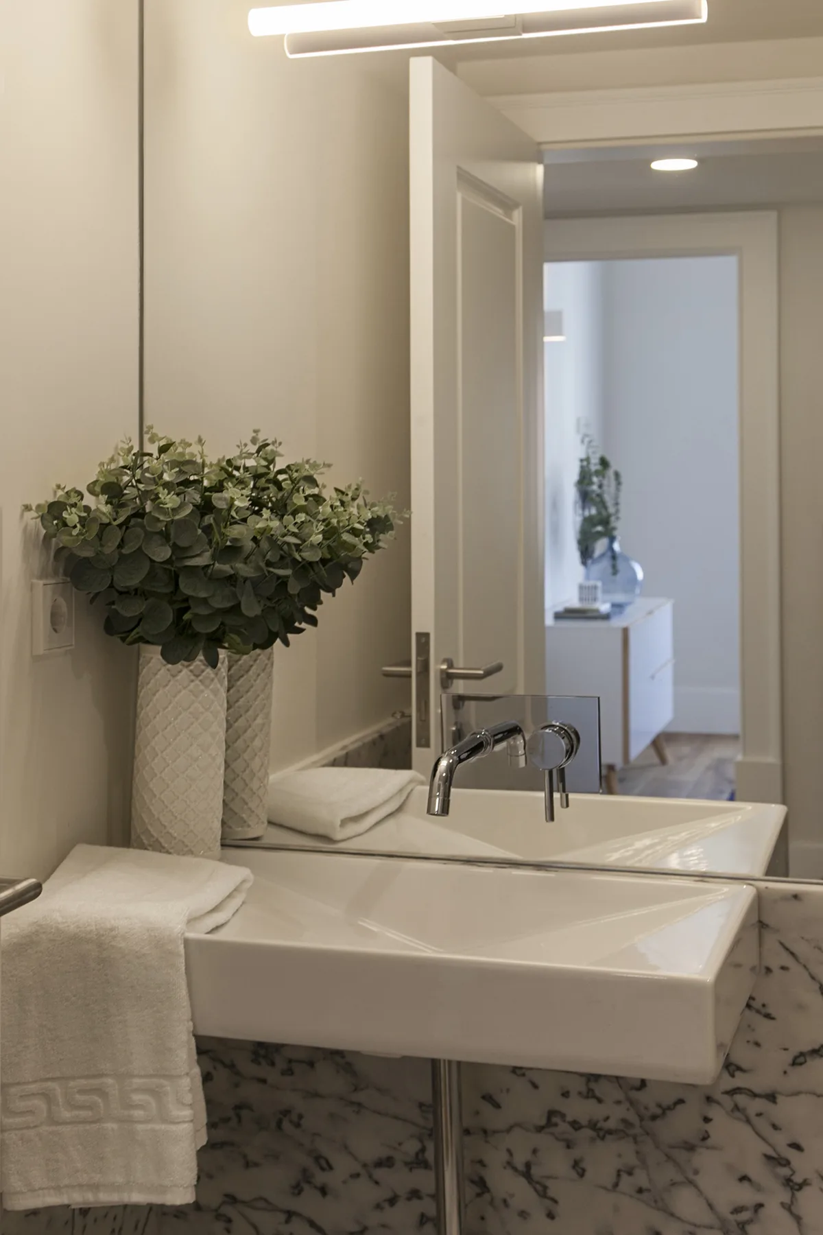 A bathroom vanity with a white basin, folded towels, and a vase of greenery.