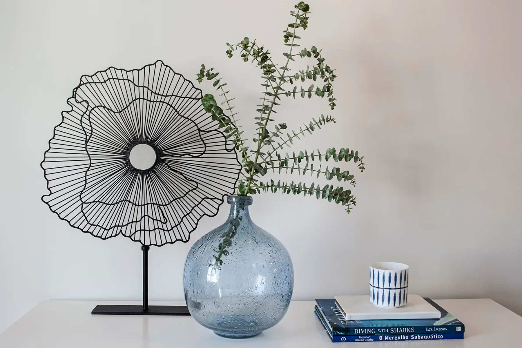 A decorative wire sculpture and leafy branches sit beside stacked books on a table.