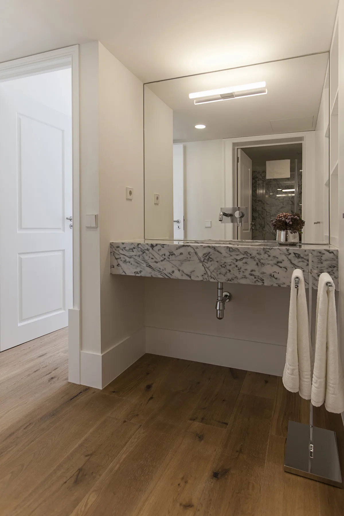 A bathroom vanity with a wide mirror, marble-patterned countertop, and hanging towels.
