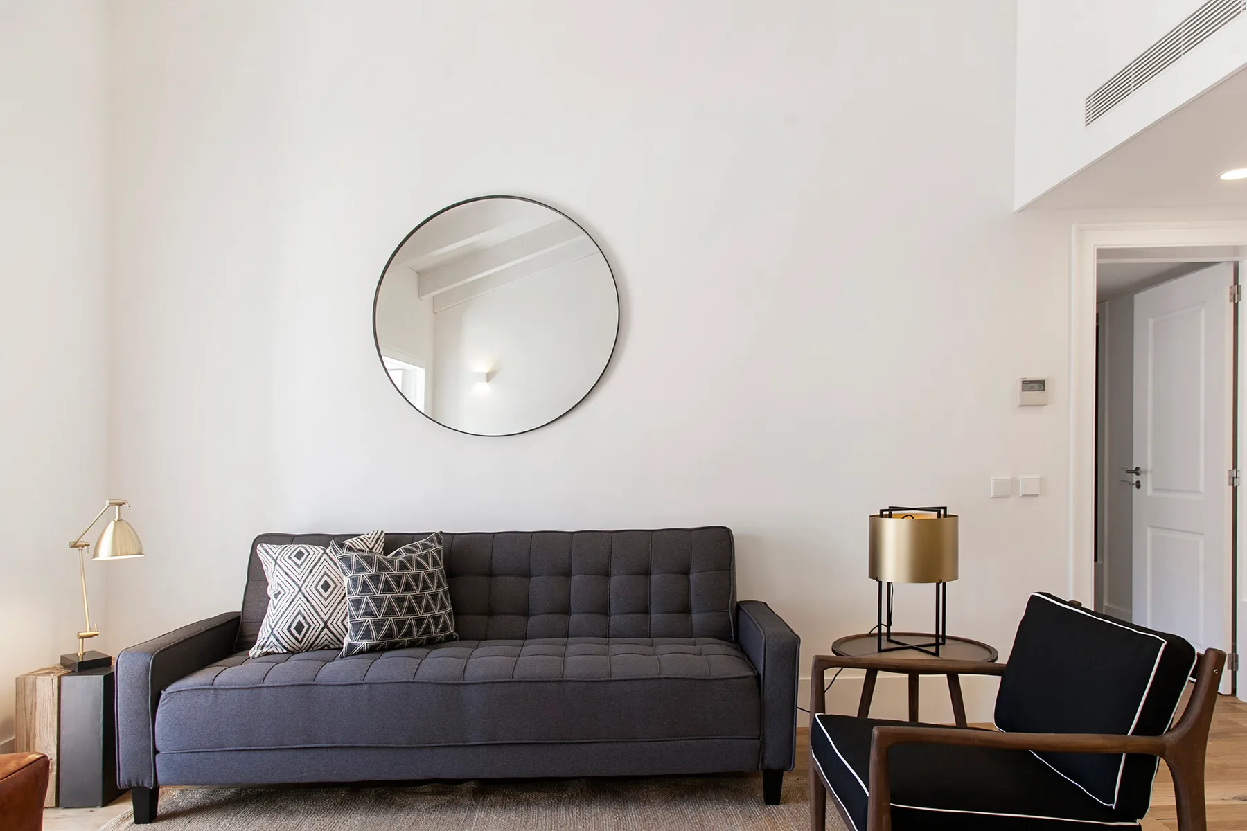 Living room with dark seating, a round wall mirror, and a floor lamp.