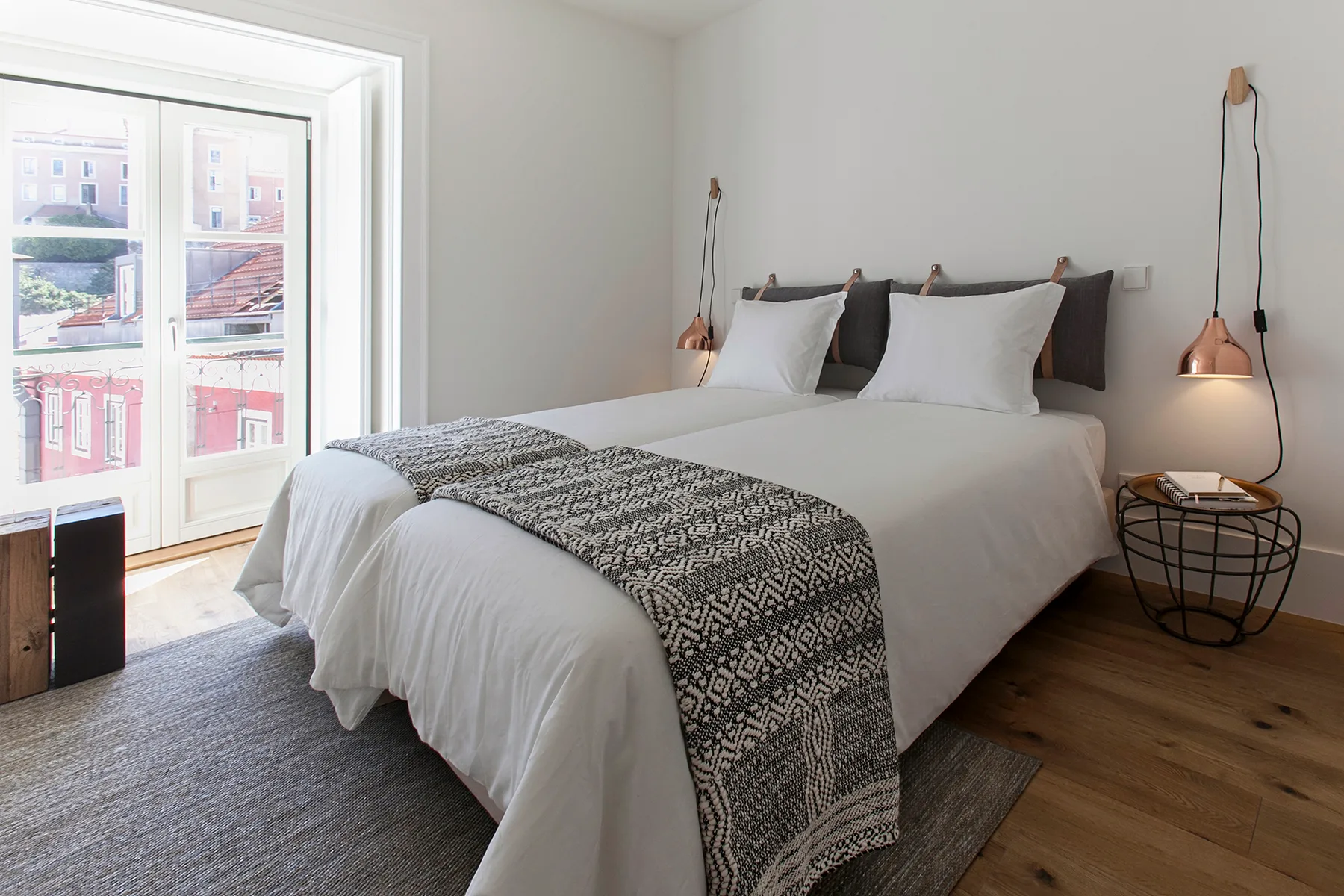 A bright bedroom with white bedding and a patterned blanket at the foot of the bed.