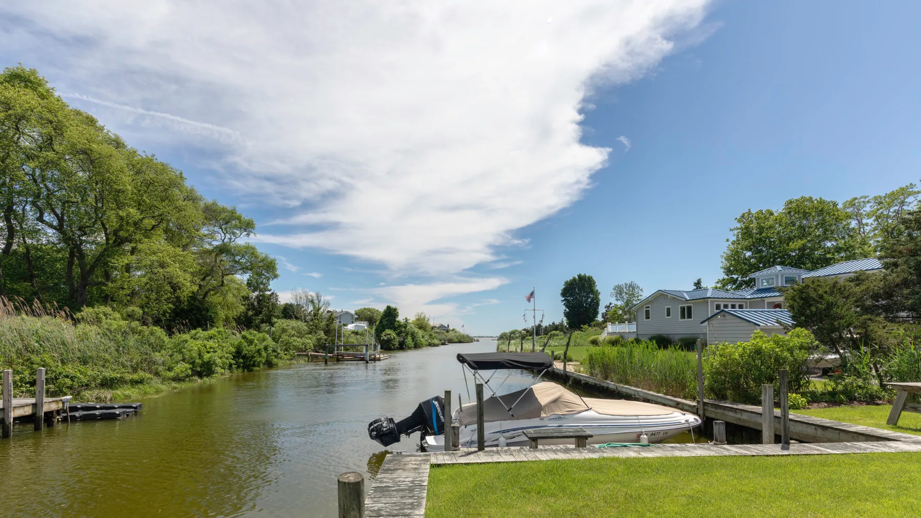 A waterside dock and moored boats sit beside a green lawn and houses.