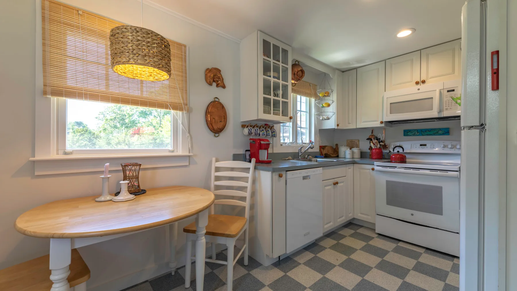 A bright kitchen with white cabinets, a checkered floor, and a small dining table.