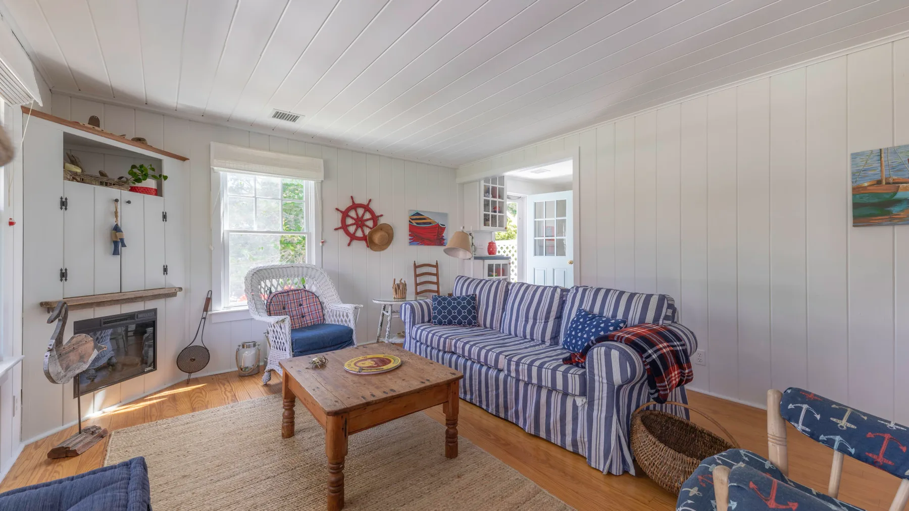 A bright living room with striped seating, a wooden coffee table, and nautical decorations.