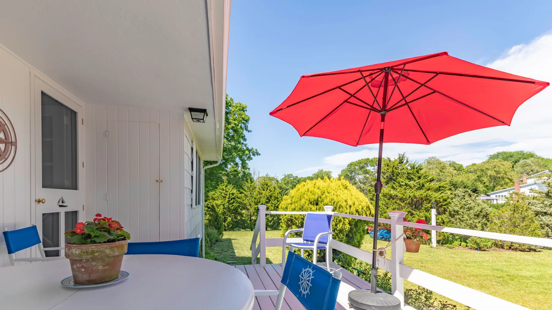 A patio seating area with a red umbrella overlooks a green lawn.