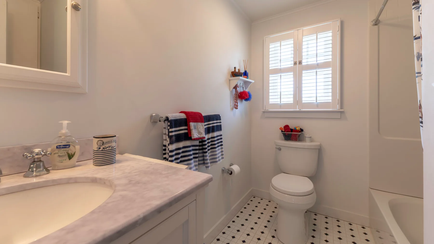A bright bathroom with a vanity, toilet, and window with shutters.