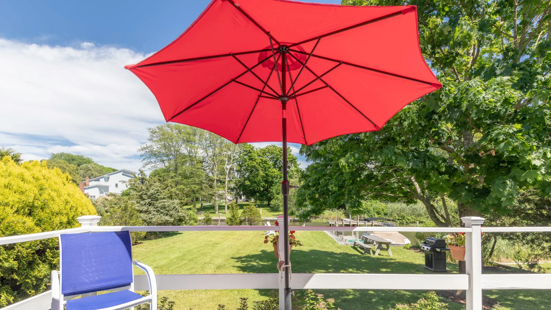 An outdoor patio overlooks a green lawn beneath a large red umbrella.
