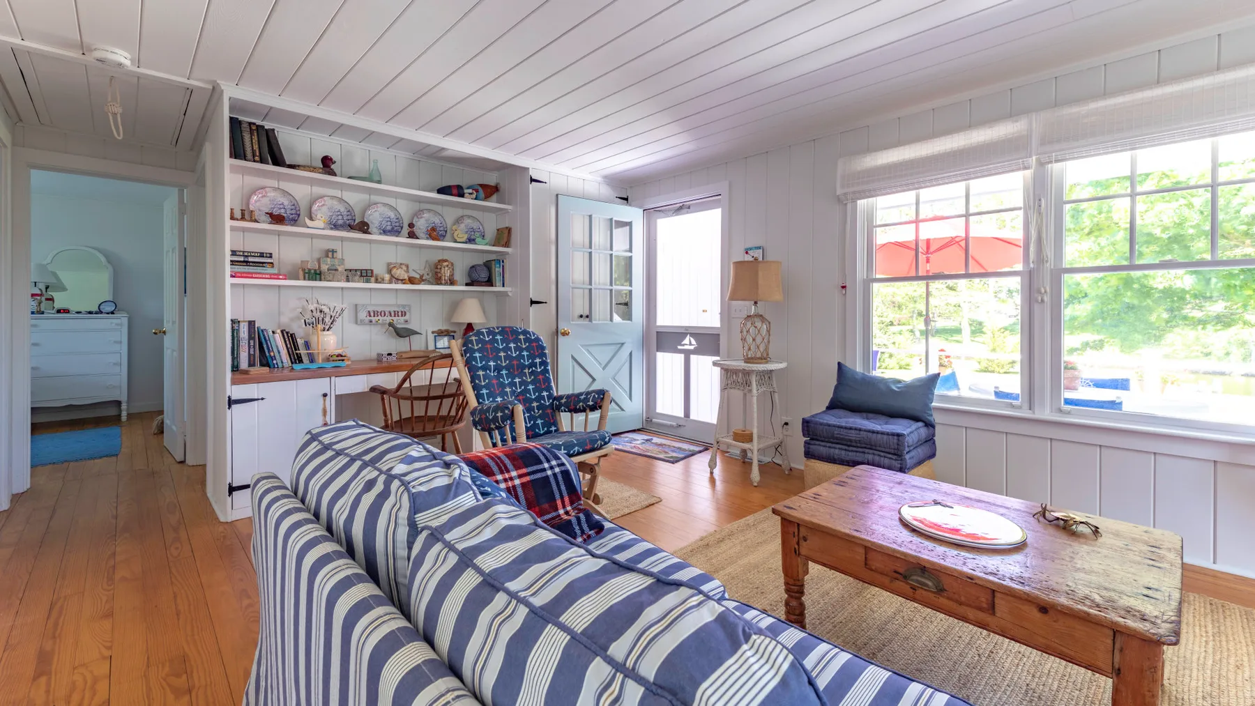 A bright living room with striped seating, a wooden coffee table, and large windows.