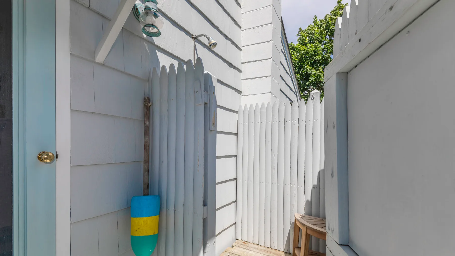 A narrow outdoor passage between white walls and a white picket gate.