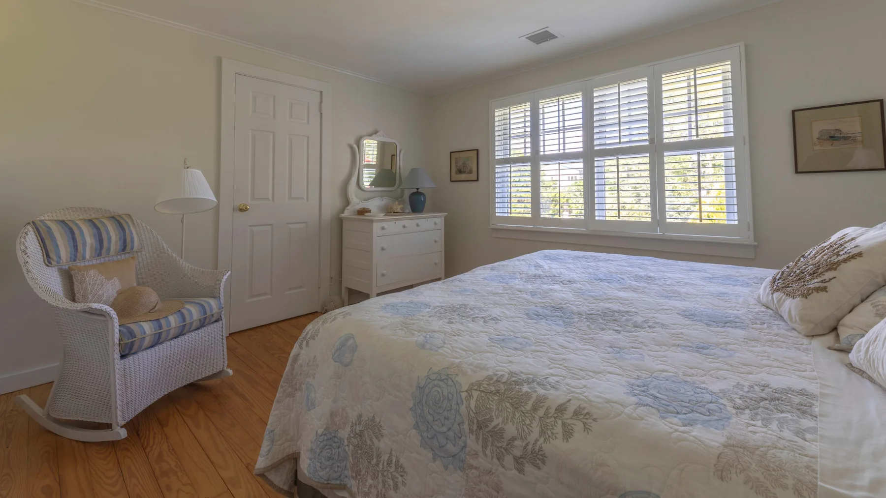 A bedroom with a large bed, a dresser, and broad windows with shutters.