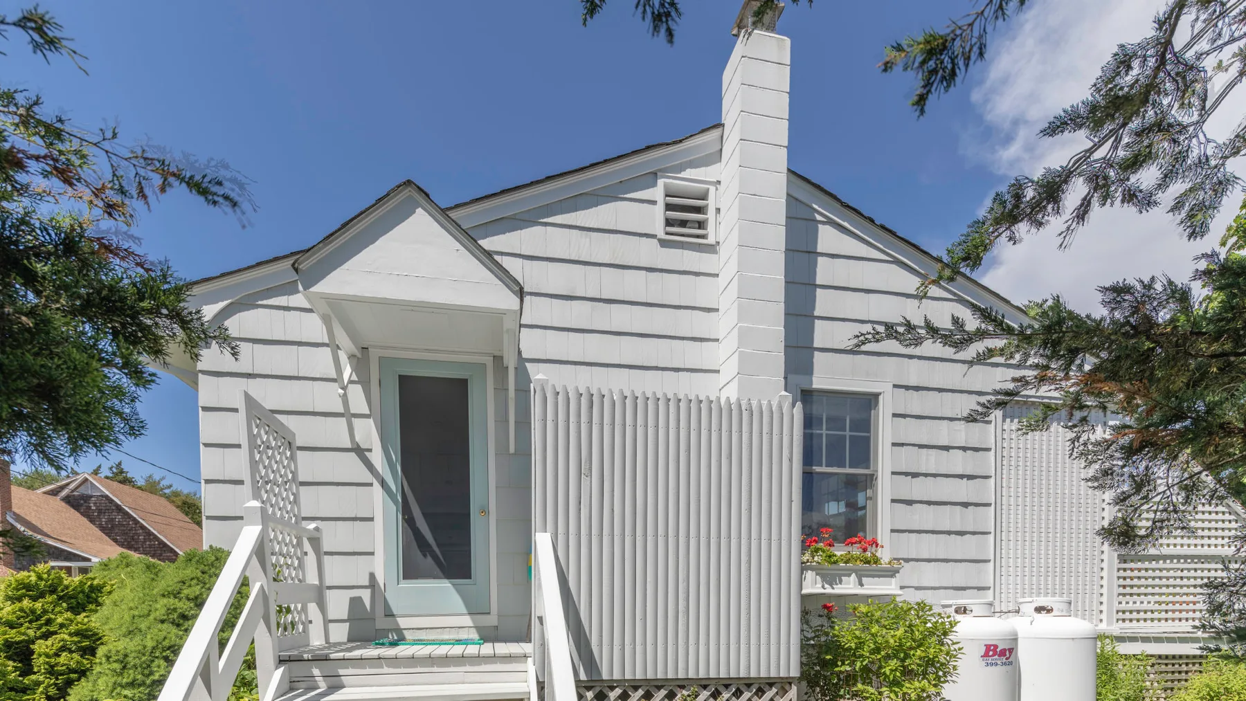 A white house exterior with a front porch and leafy trees.