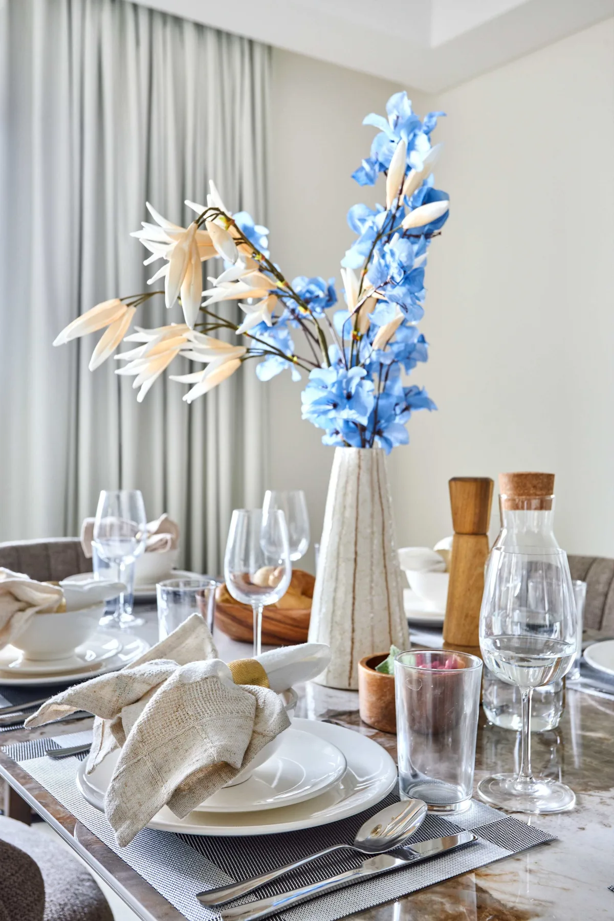 Una mesa de comedor está puesta con platos, cristalería y un florero con flores.