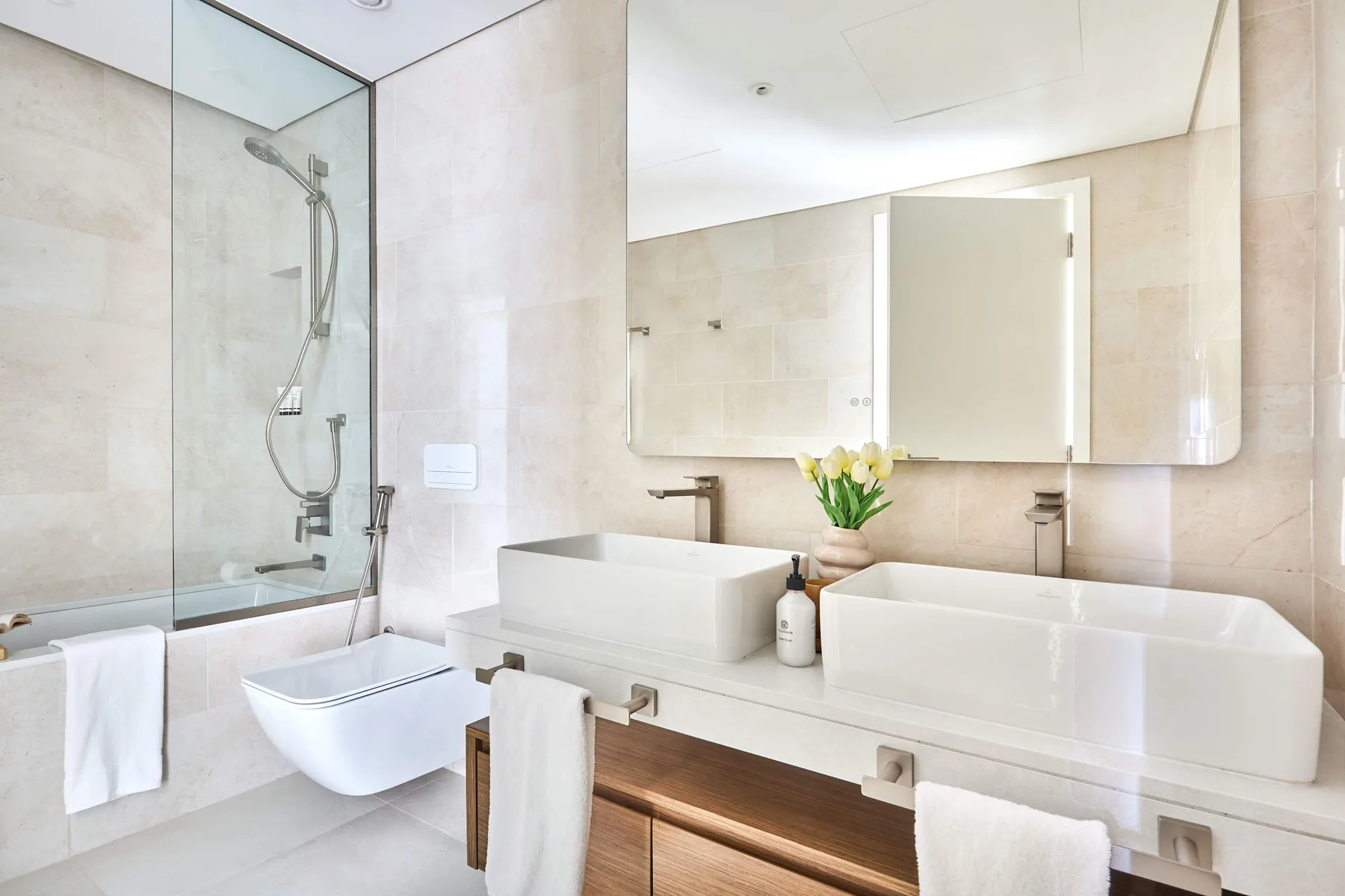 Un baño luminoso con ducha de vidrio, bañera y tocador con dos lavabos.