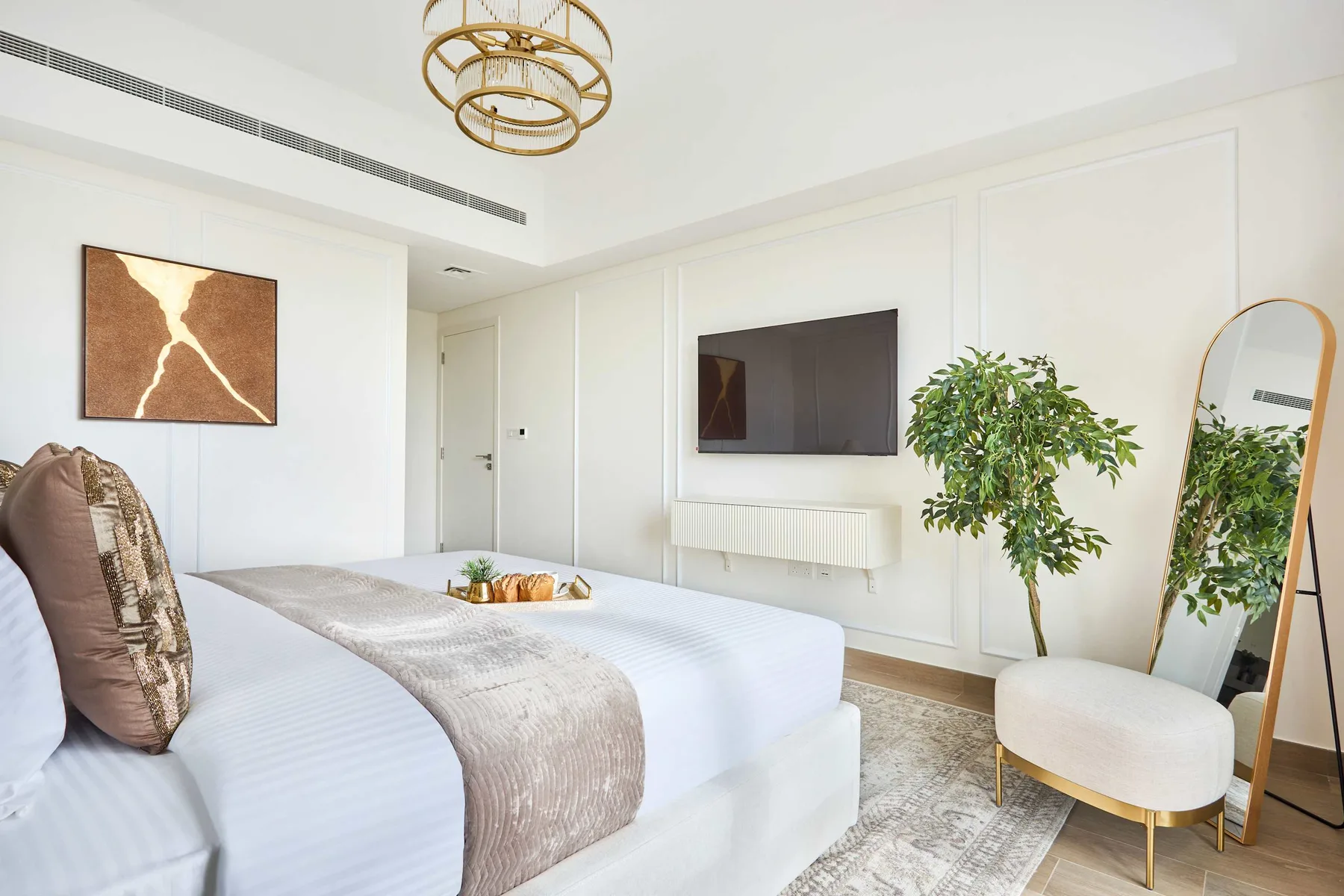 Un dormitorio luminoso con una cama bien hecha, un televisor en la pared y una planta frondosa.