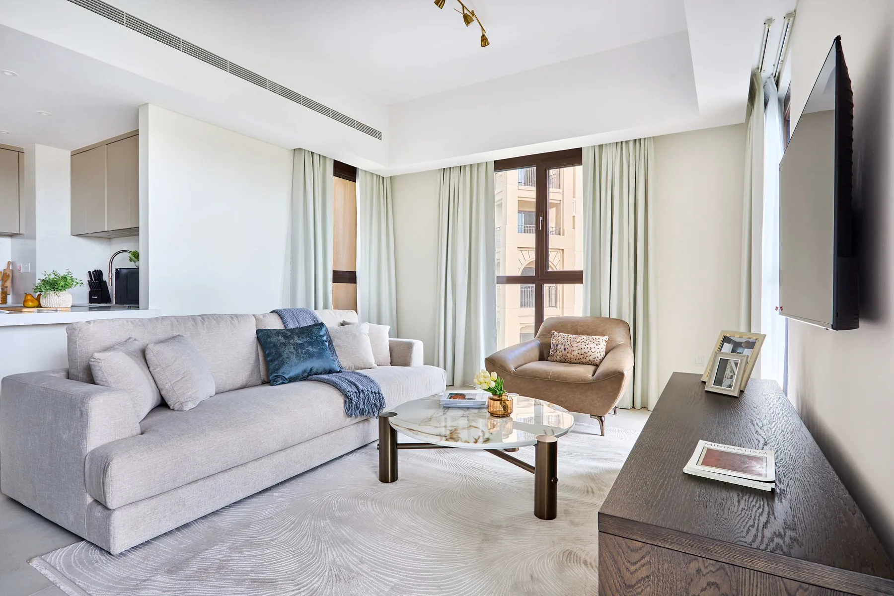 Una sala luminosa con asientos, una mesa de centro de vidrio y grandes ventanas con cortinas.