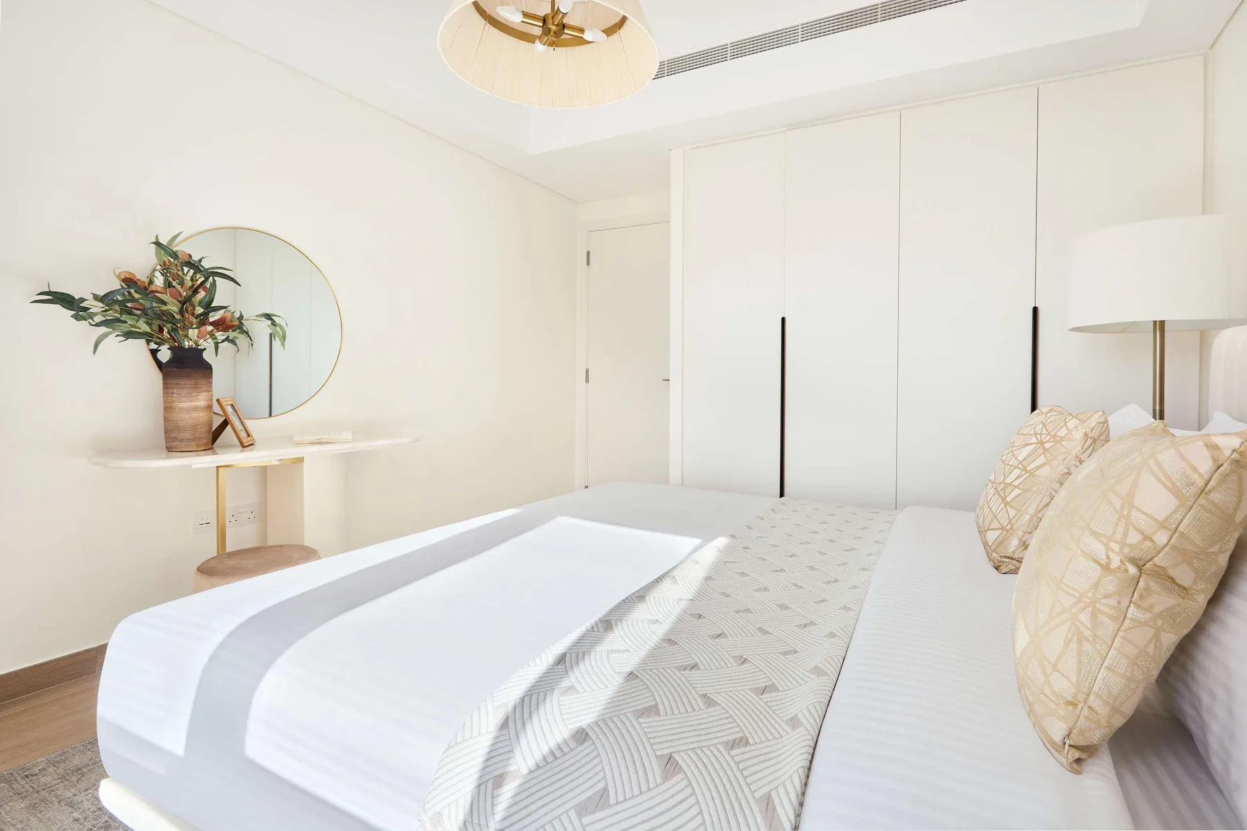 Un dormitorio luminoso con una cama arreglada y una mesita con flores.