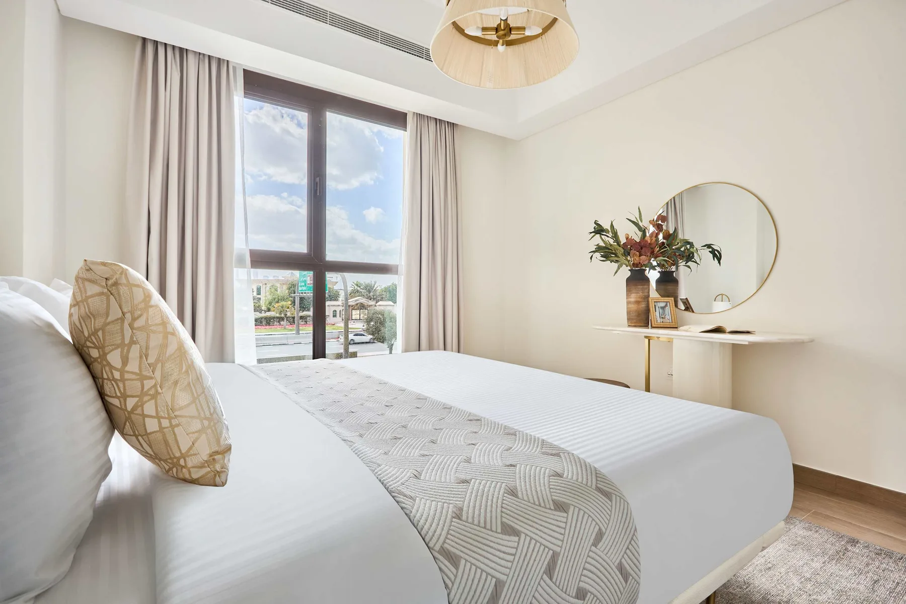 Un dormitorio luminoso con una ventana amplia, cortinas claras y una cama bien tendida.