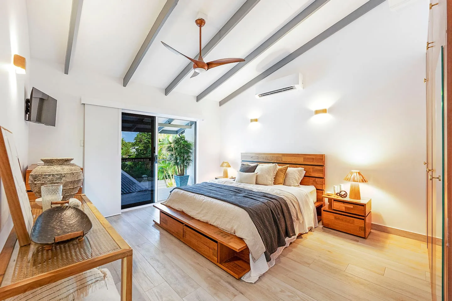 A bright bedroom with a large bed and sliding glass doors opening to greenery.