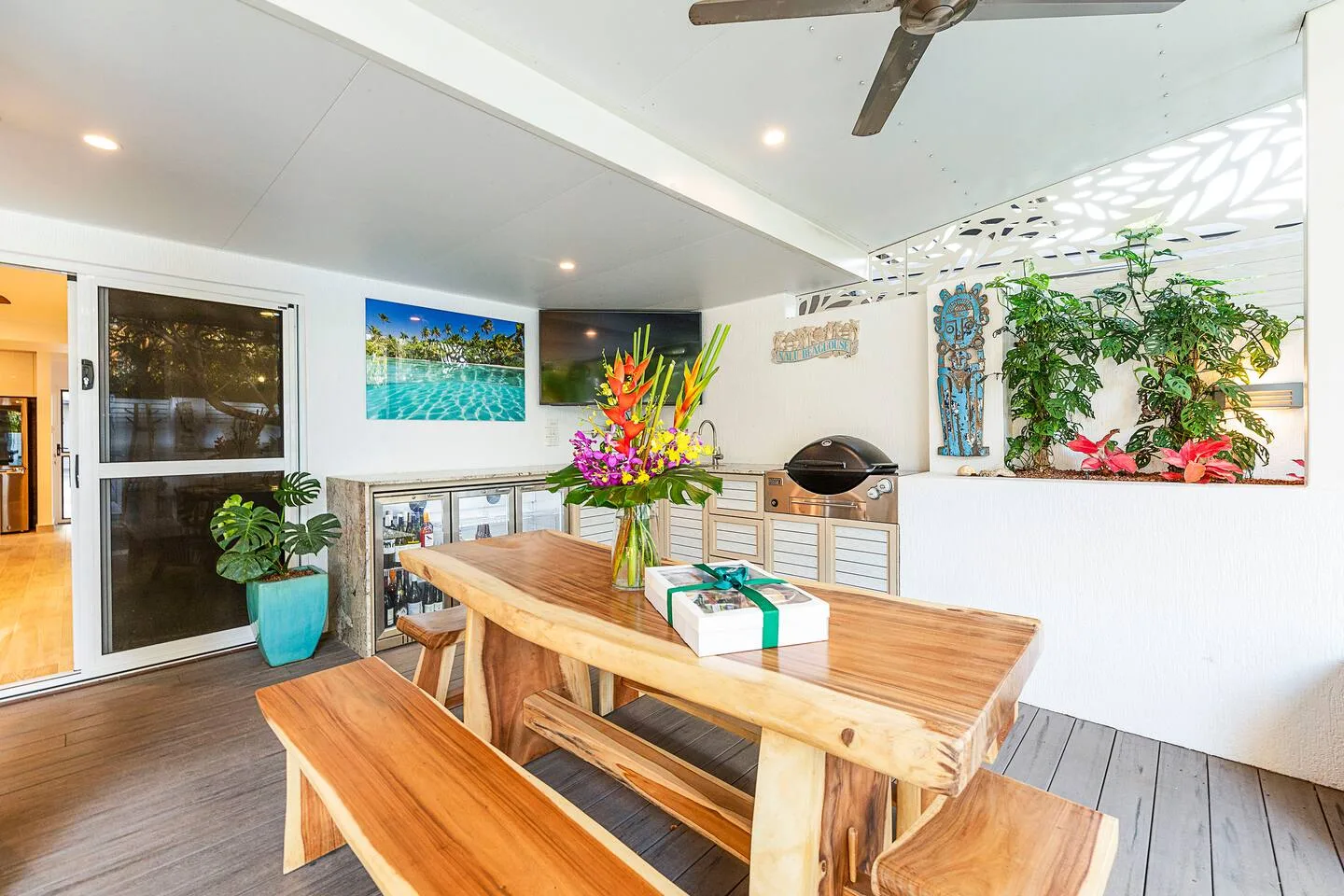 A covered outdoor dining area has a wooden table, benches, and a barbecue.