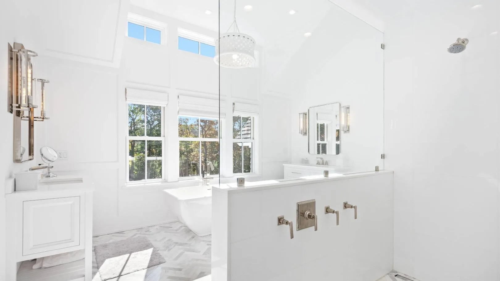 Un baño blanco y luminoso tiene una bañera, un amplio lavabo y grandes ventanas.