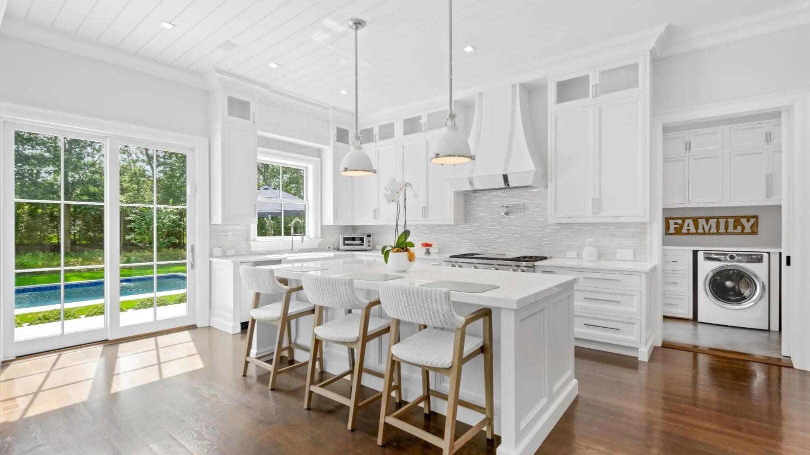 Una cocina blanca y luminosa con una isla y grandes puertas de vidrio que dan al jardín.