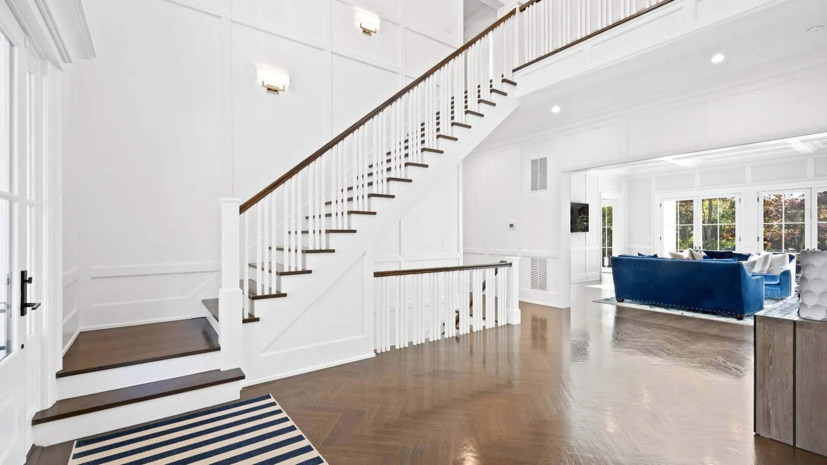 Una luminosa sala de estar se abre junto a una escalera, con asientos azules al fondo.