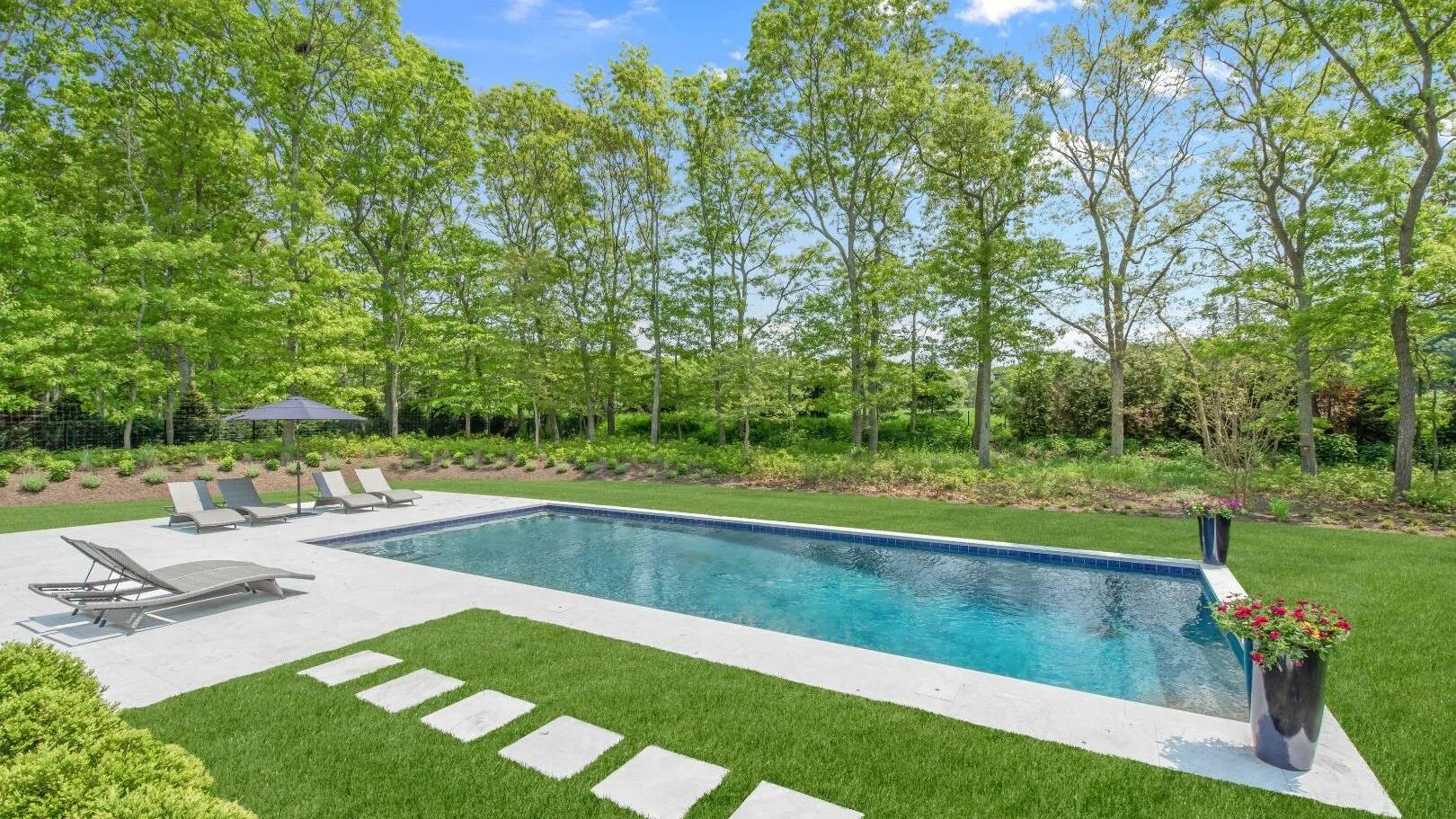 Una piscina exterior junto a un patio pavimentado y un césped verde.