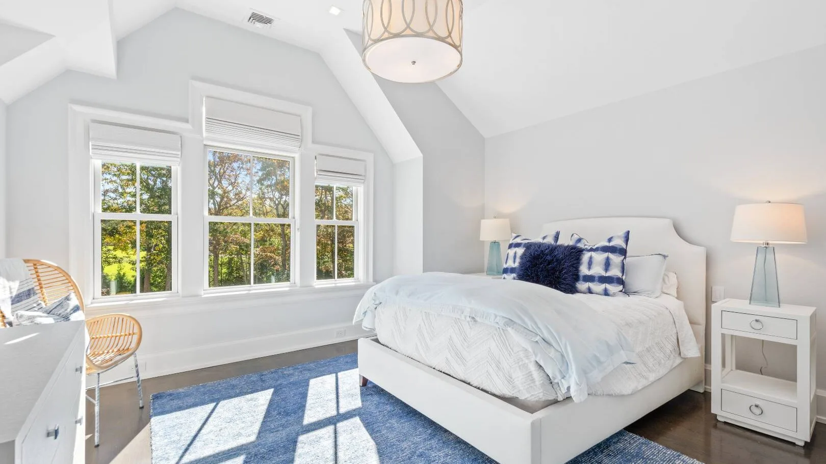 Un dormitorio luminoso con una cama, ropa de cama blanca y ventanas grandes.
