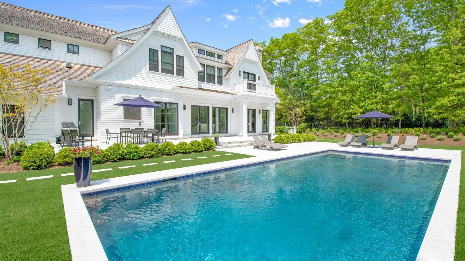 Una piscina grande está junto a una casa blanca y un césped verde.