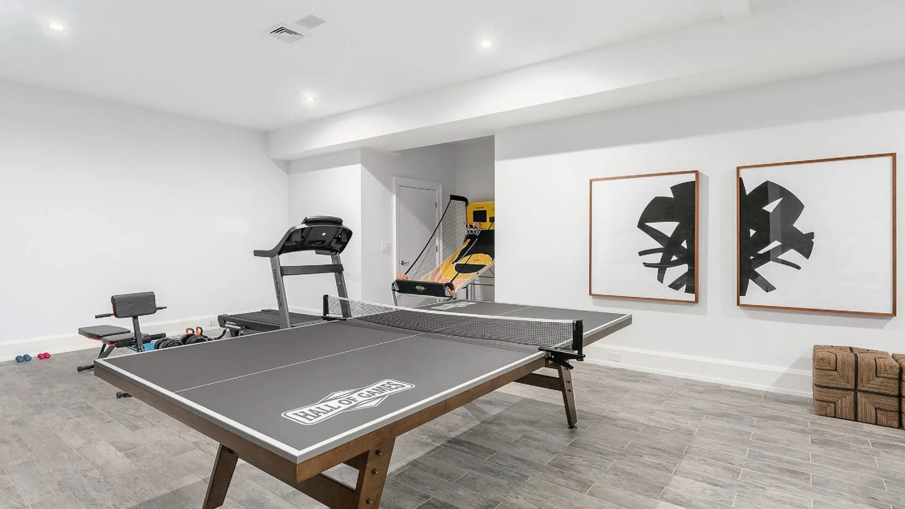 Una sala recreativa con una mesa de ping-pong, equipo de ejercicio y arte abstracto enmarcado.