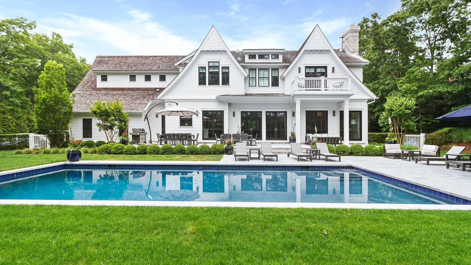 Una gran casa blanca se alza detrás de una piscina y un césped.