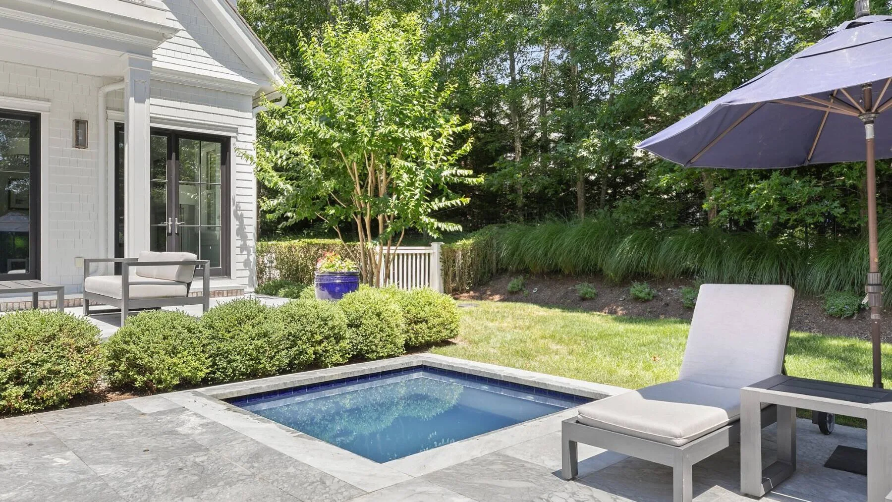 Un patio exterior con una pequeña piscina rectangular, asientos y un jardín.