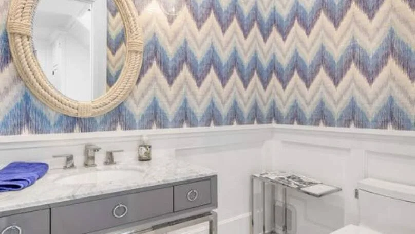 Un lavabo de baño con una pared estampada y un espejo redondo.