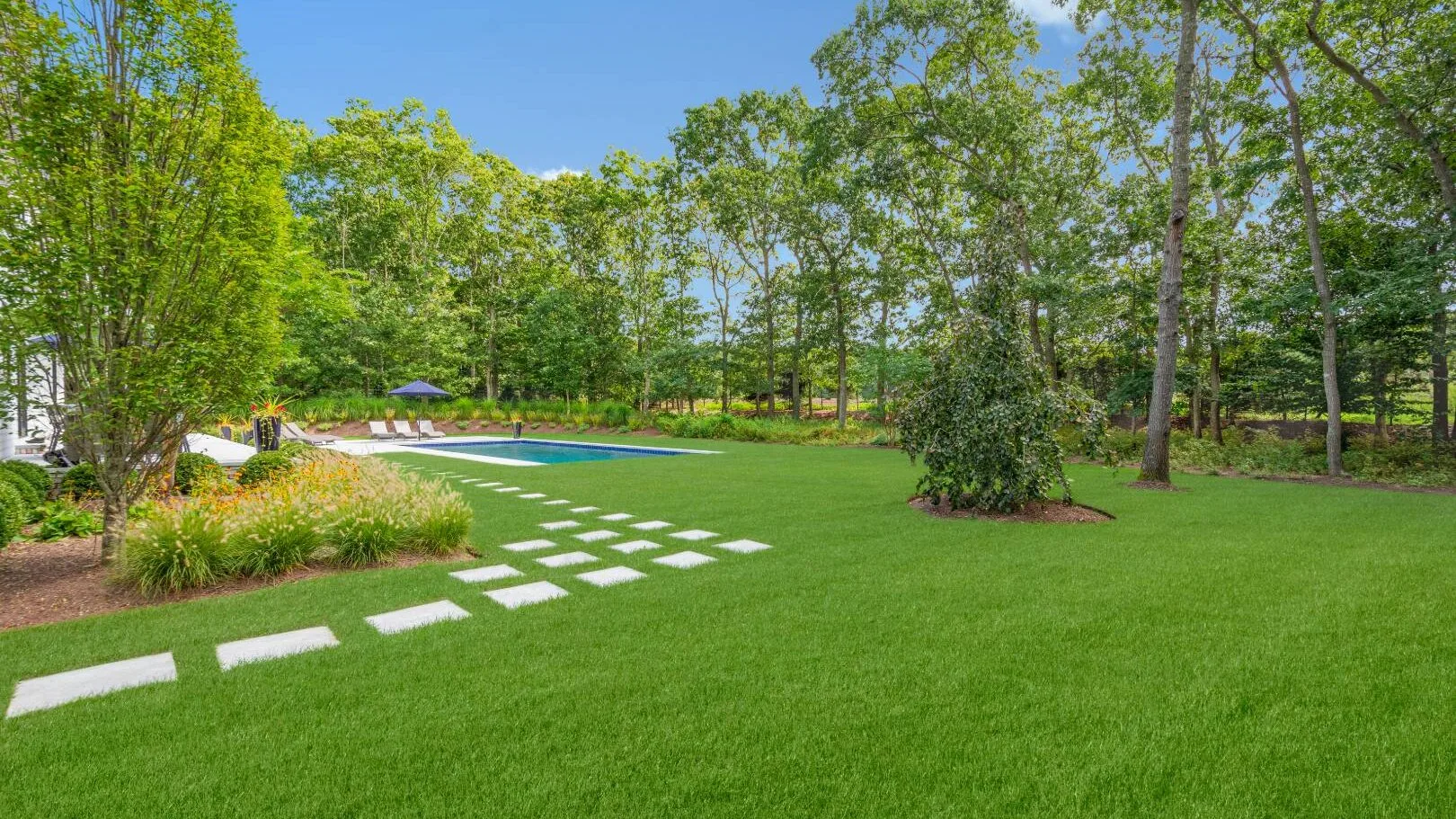 Un jardín con césped, piedras para caminar y una piscina.
