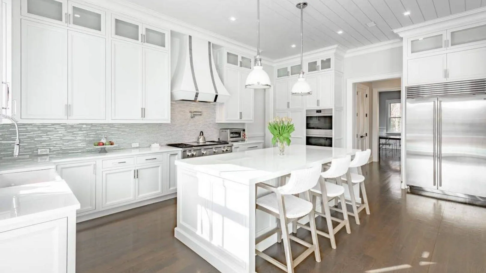 Una cocina blanca y luminosa con una isla grande y asientos.