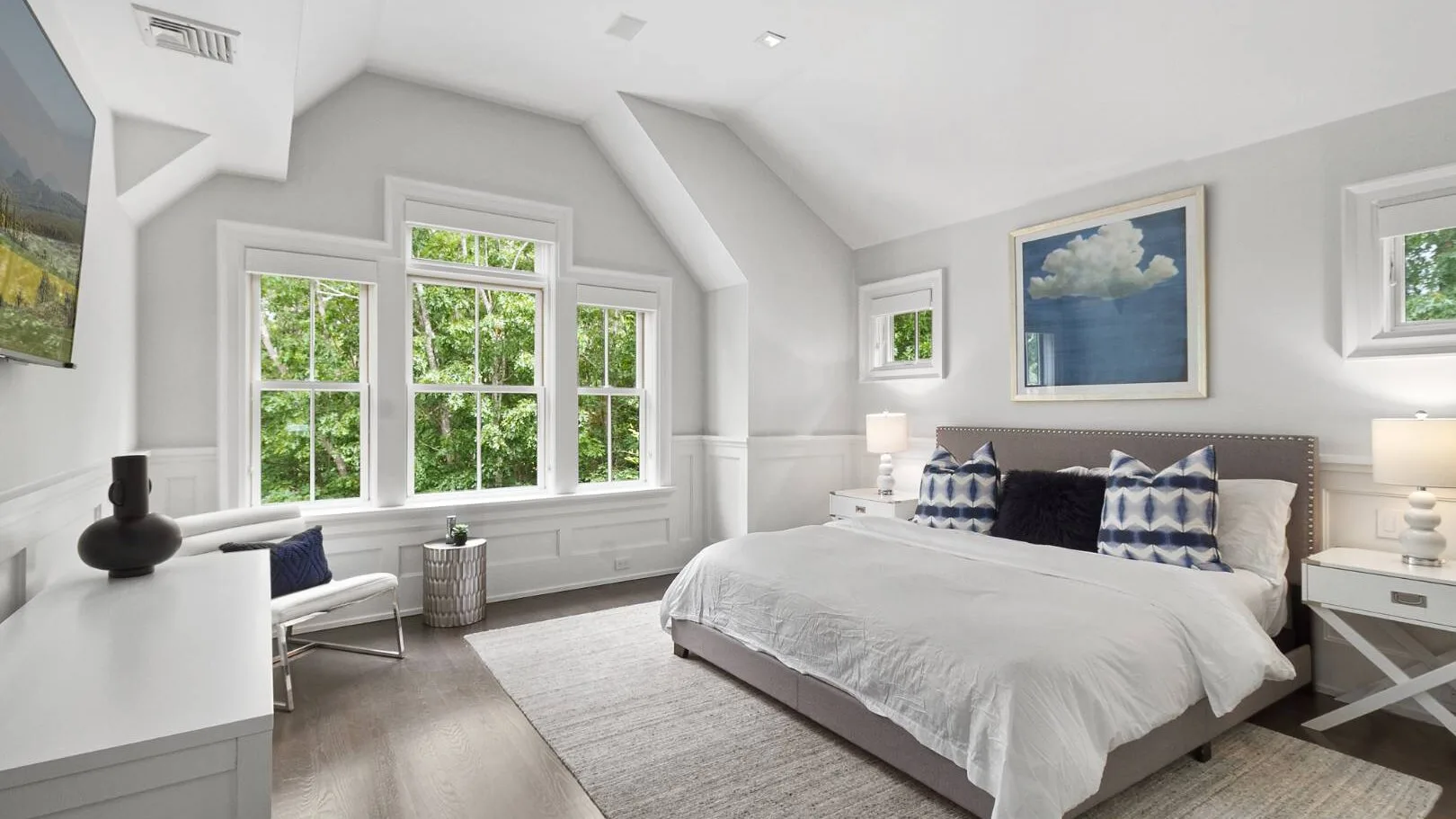 Un dormitorio luminoso con una cama grande y varias ventanas con vistas a la vegetación.