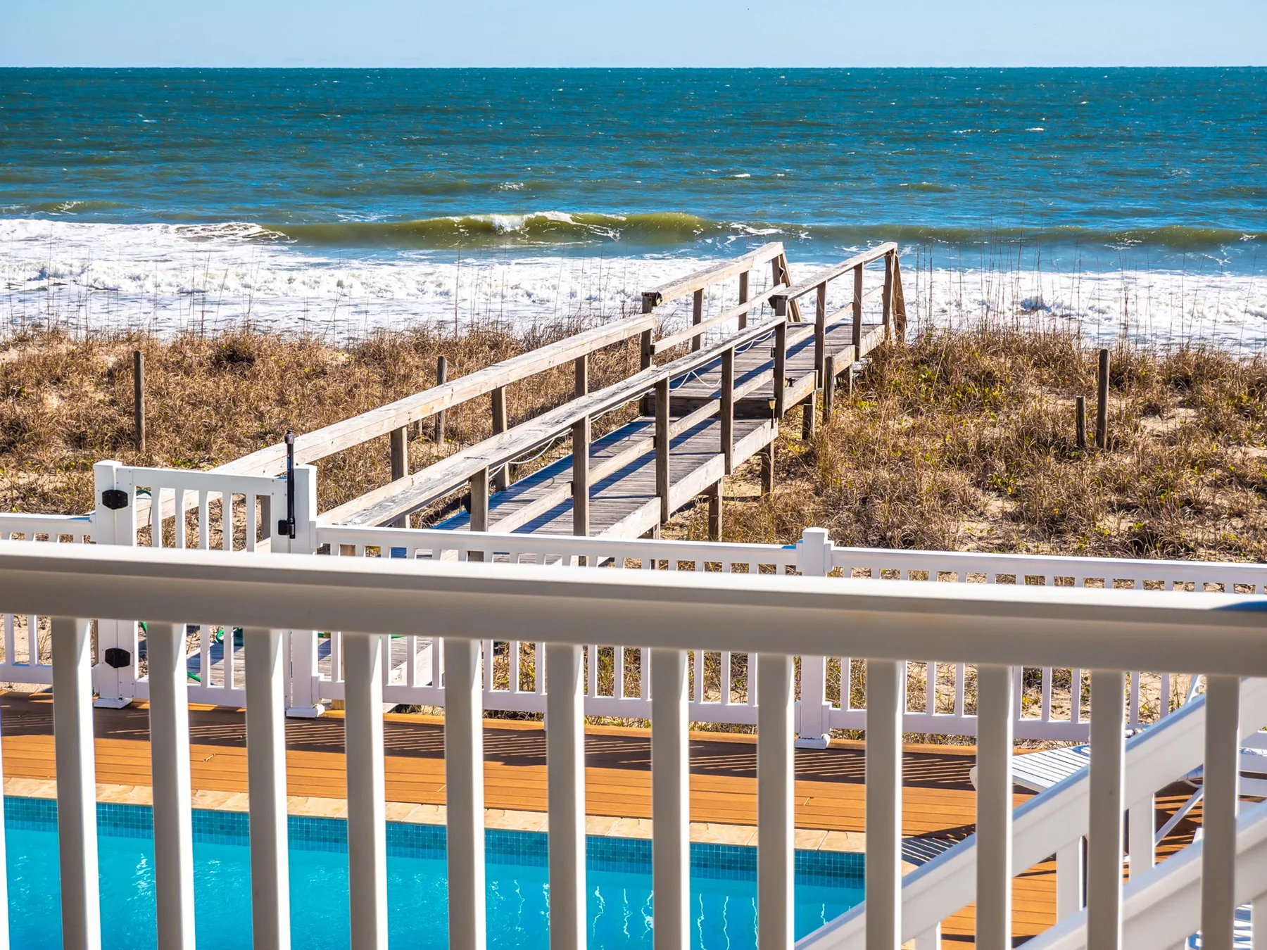 A beach access walkway leads toward the ocean beside a swimming pool.