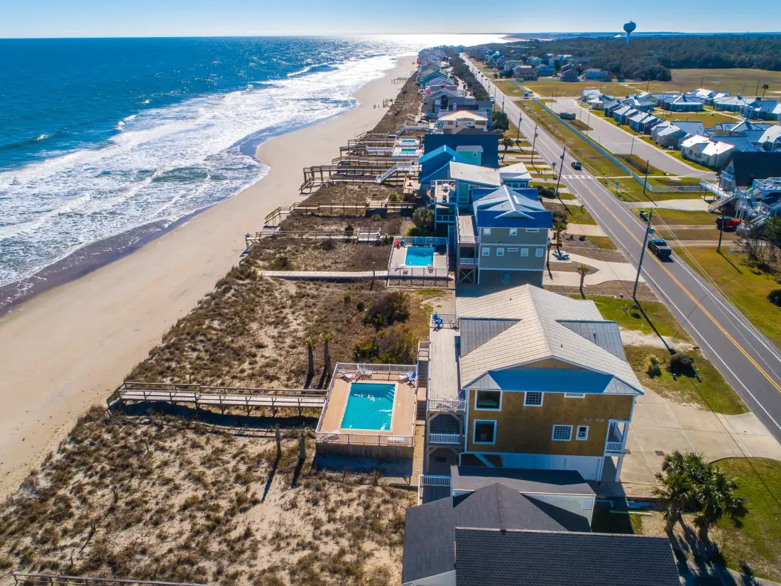 Vista aérea de casas junto a una playa de arena y una carretera costera.