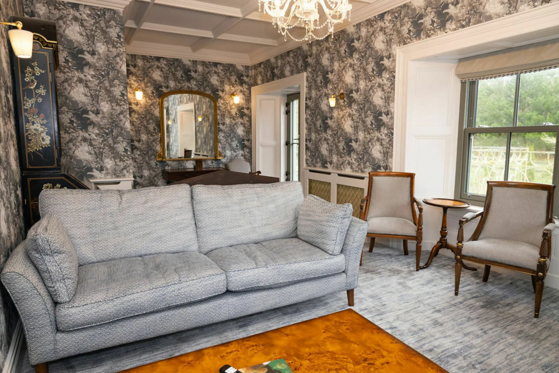 A sitting room with a gray sofa and chairs beside a large window.