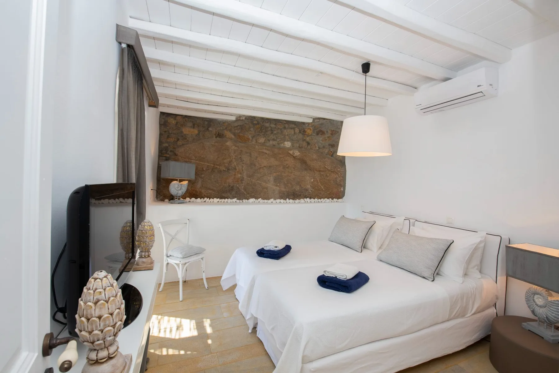 Un dormitorio con una cama grande, ropa de cama blanca y una pared de piedra vista.