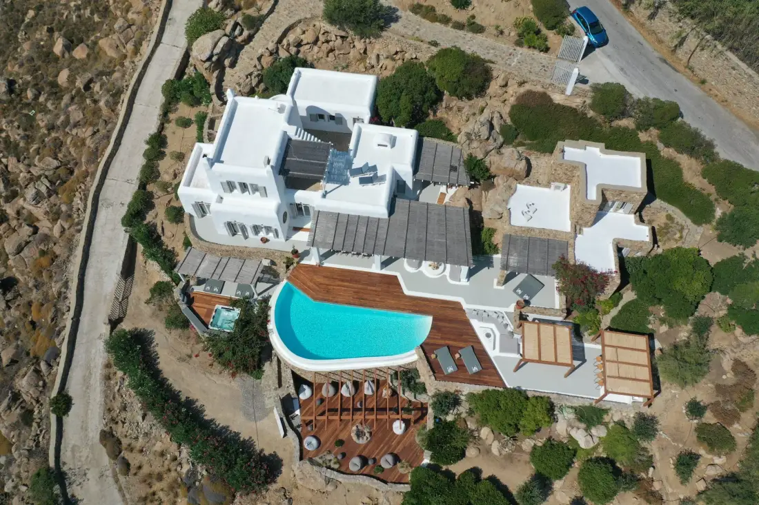 Aerial view of a white villa with a curved swimming pool and surrounding terraces.