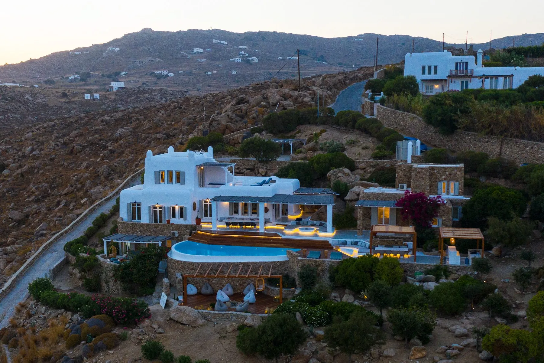 Una villa en la ladera con una piscina iluminada y terreno rocoso alrededor.