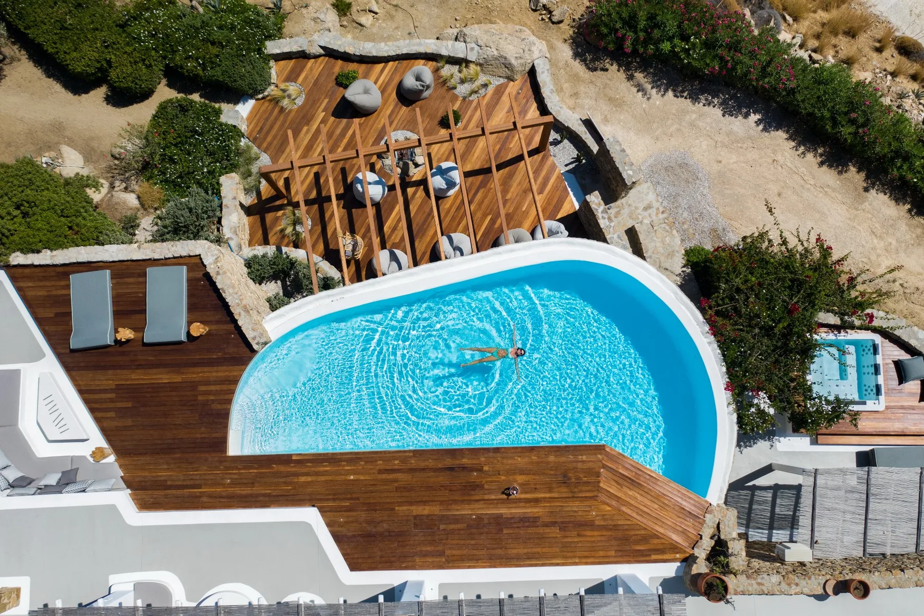 Una piscina al aire libre junto a una terraza de madera y una zona de descanso.