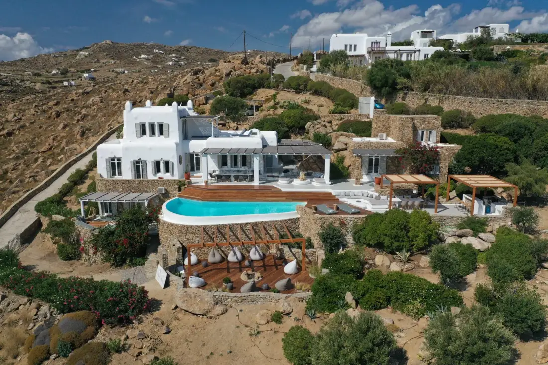 A hillside villa with a turquoise pool and outdoor seating.