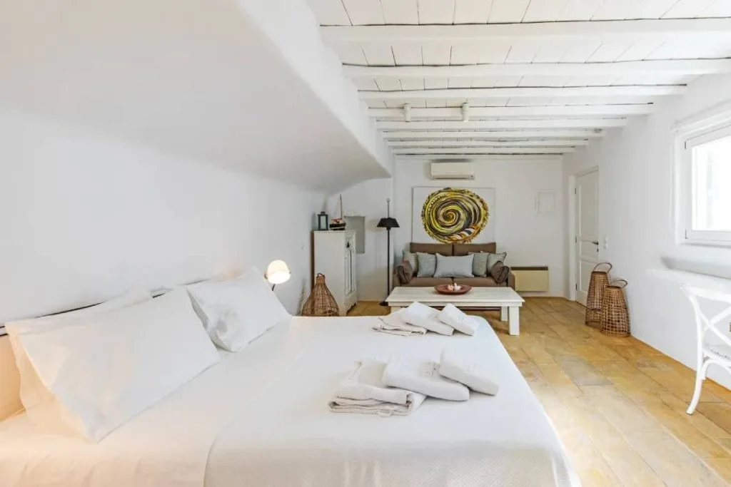 Un dormitorio luminoso con una cama grande y una zona de estar al fondo.