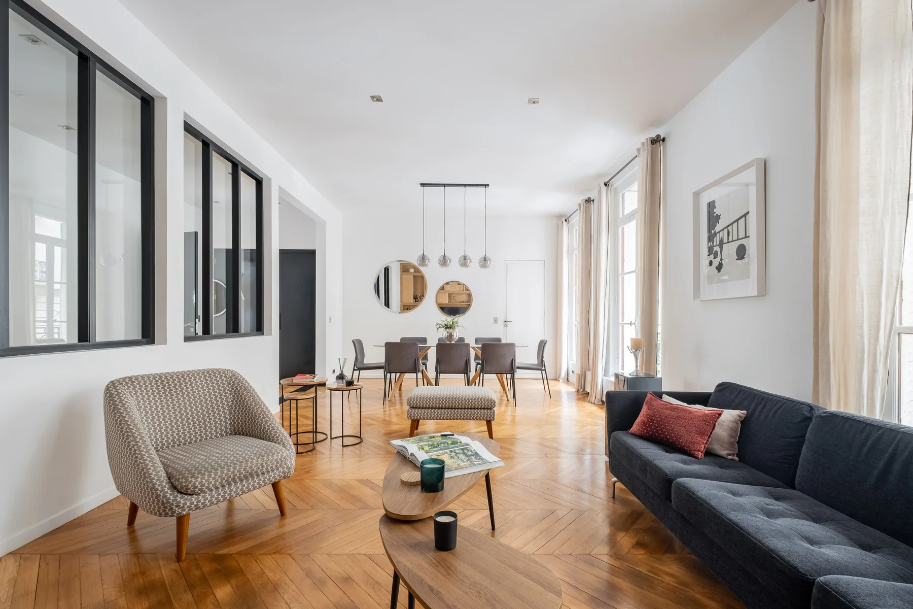 Una sala de estar luminosa con asientos, mesas de centro y ventanas altas.