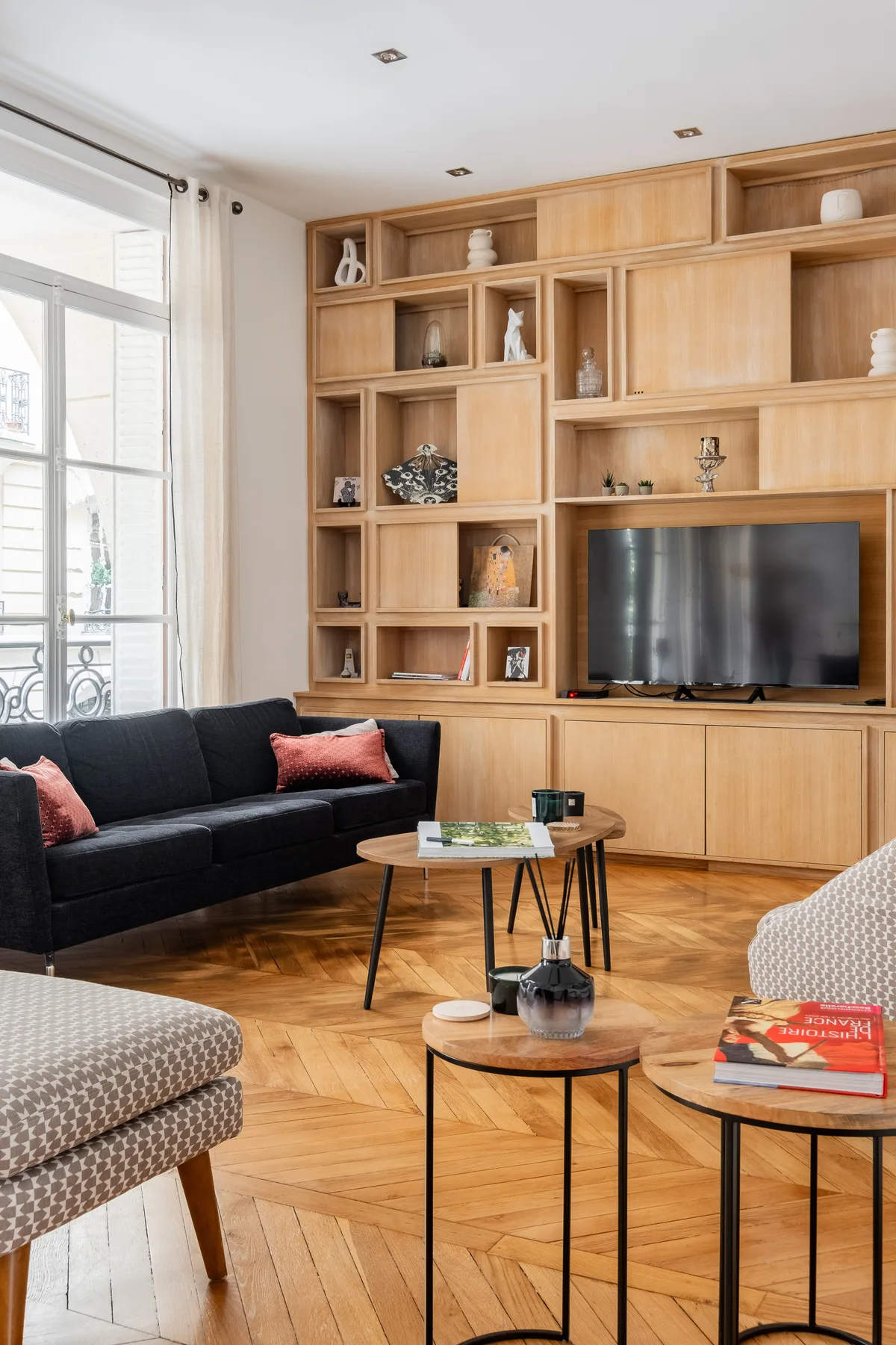 Una sala de estar con un sofá negro, estanterías de madera y un televisor.