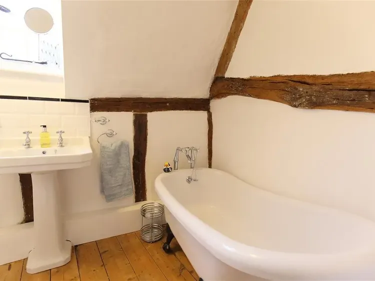 A bathroom with a freestanding bathtub and sink beneath exposed wooden beams.