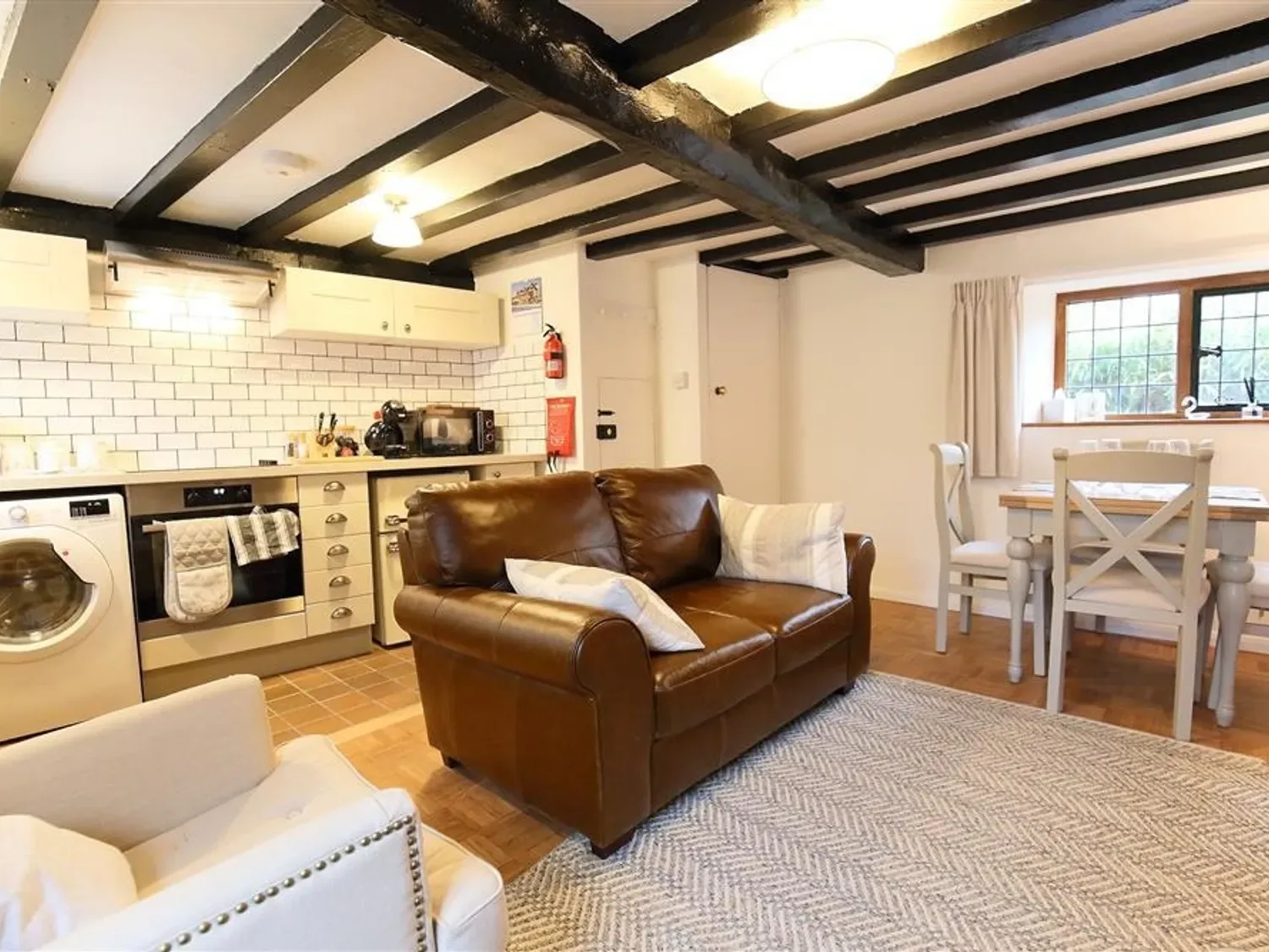 A living and dining area with a brown leather sofa beside a dining table and kitchen.