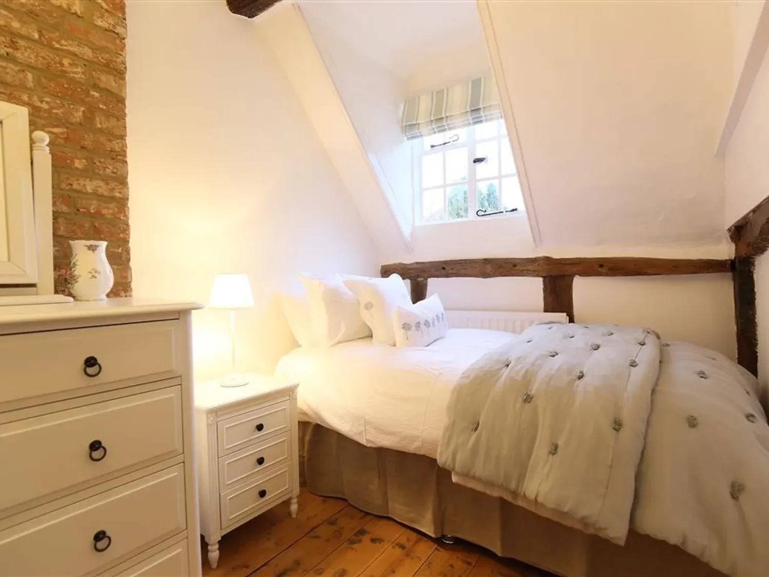 A bedroom with a bed pillows bedside table lamp chest of drawers and a window at One Masons Court in Stratford upon Avon